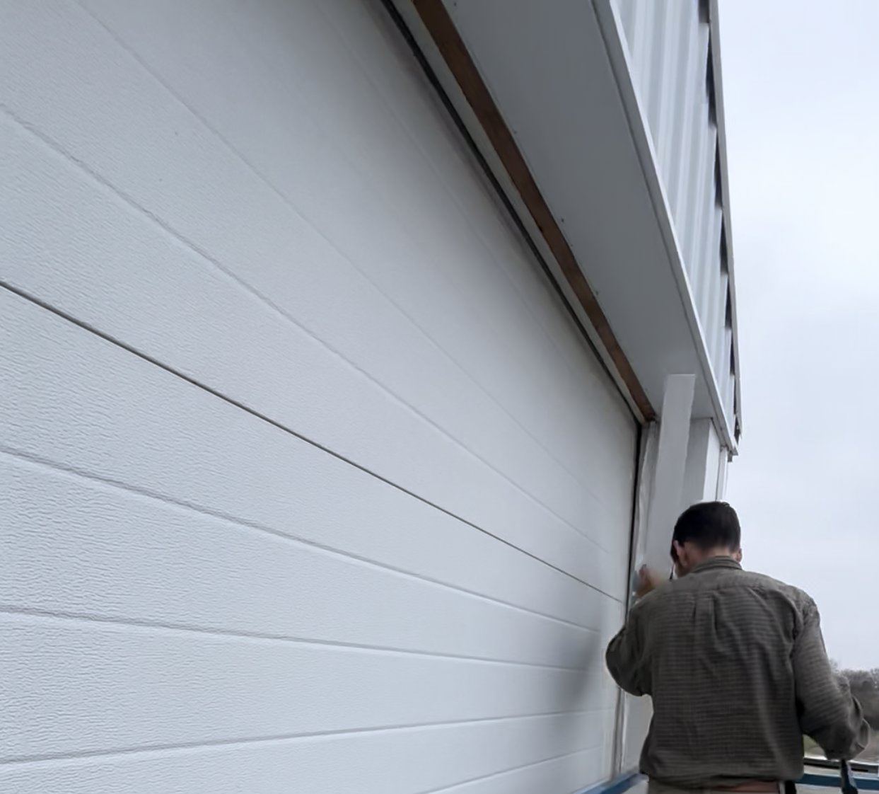 PRO-Link technician sealing a commercial overhead door from a lift